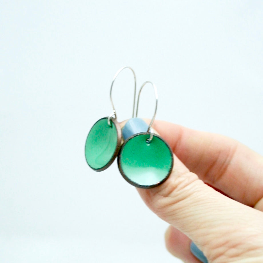 a person holding a pair of green earrings