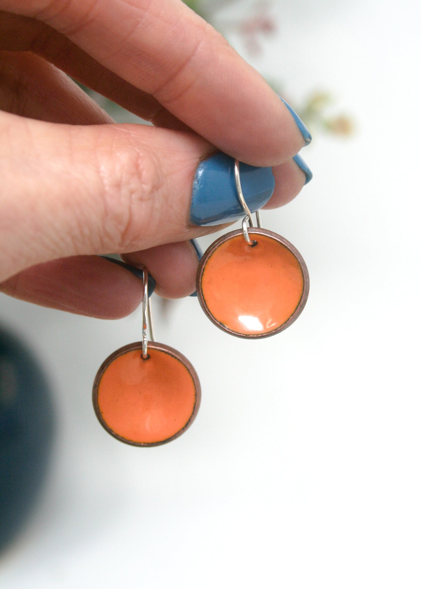 a person holding a pair of orange and blue earrings